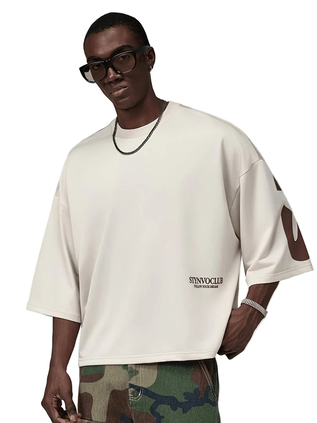 Oversized heren T-shirt in khaki, voorkant met zwarte STYNVOCLUB-letterprint, ronde hals, verlaagde schouders en grafische mouwprint op witte achtergrond.