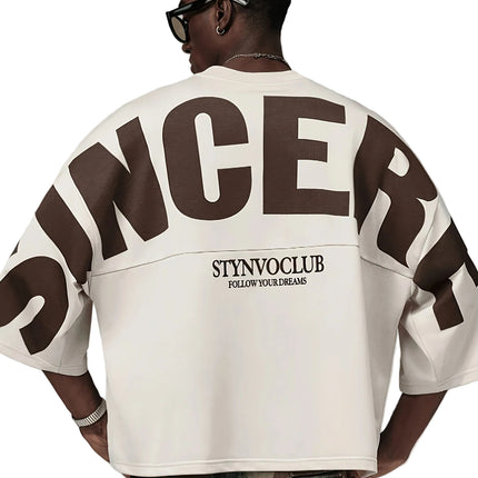 Oversized heren T-shirt in khaki, voorkant met zwarte STYNVOCLUB-letterprint, ronde hals, verlaagde schouders en grafische mouwprint op witte achtergrond.
