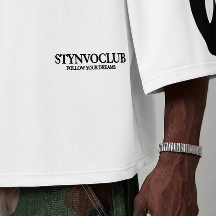 Oversized heren T-shirt in khaki, voorkant met zwarte STYNVOCLUB-letterprint, ronde hals, verlaagde schouders en grafische mouwprint op witte achtergrond.