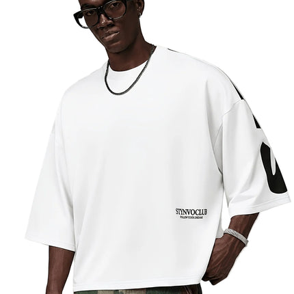 Oversized heren T-shirt in khaki, voorkant met zwarte STYNVOCLUB-letterprint, ronde hals, verlaagde schouders en grafische mouwprint op witte achtergrond.