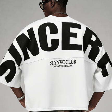 Oversized heren T-shirt in khaki, voorkant met zwarte STYNVOCLUB-letterprint, ronde hals, verlaagde schouders en grafische mouwprint op witte achtergrond.