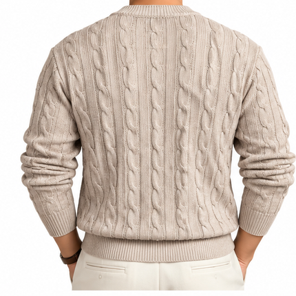 Heren kabeltrui met ronde hals, lange mouwen en klassiek kabelgebreid patroon, gedragen door een mannelijk model met een witte pantalon tegen een witte achtergrond.