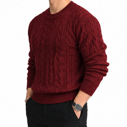 Heren kabeltrui met ronde hals, lange mouwen en klassiek kabelgebreid patroon, gedragen door een mannelijk model met een witte pantalon tegen een witte achtergrond.