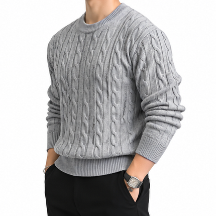 Heren kabeltrui met ronde hals, lange mouwen en klassiek kabelgebreid patroon, gedragen door een mannelijk model met een witte pantalon tegen een witte achtergrond.