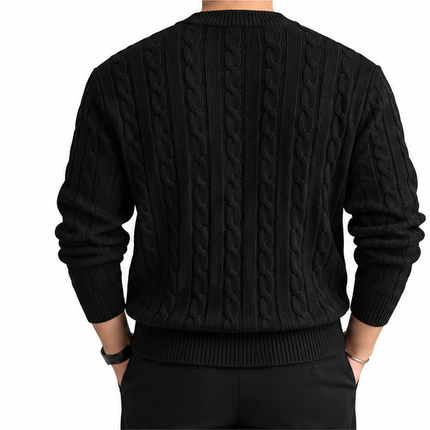 Heren kabeltrui met ronde hals, lange mouwen en klassiek kabelgebreid patroon, gedragen door een mannelijk model met een witte pantalon tegen een witte achtergrond.
